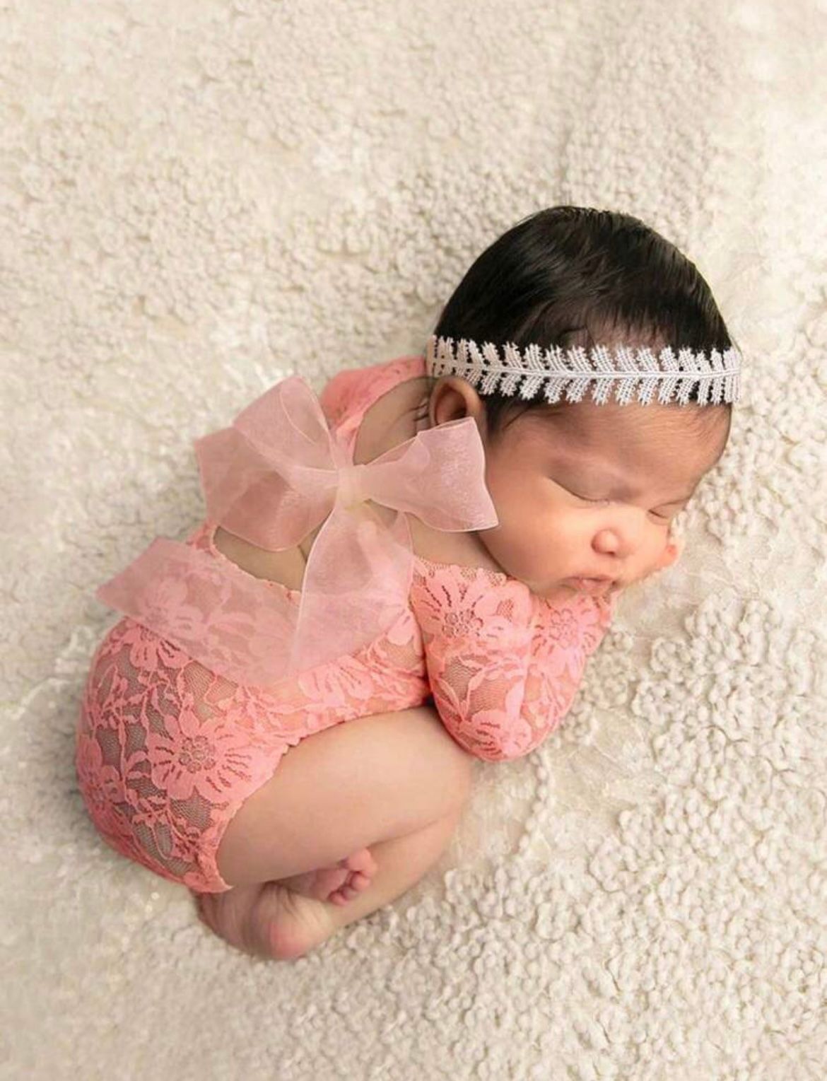 Newborn photography in pink lace outfit with pearl headband on cream backdrop.