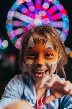 Colorful face paint and carnival lights create festive atmosphere at night.