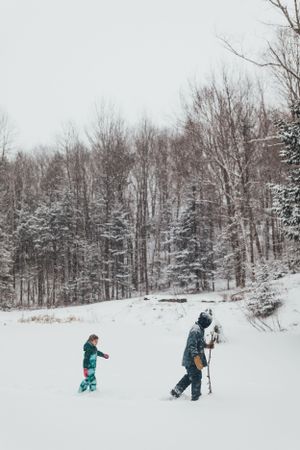 Two people snowshoeing through a snow-covered forest trail in winter.