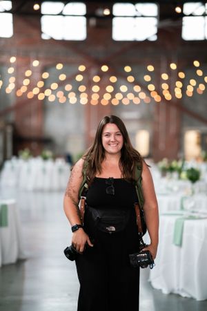 Event photographer in black dress working at an elegant reception venue with string lights.