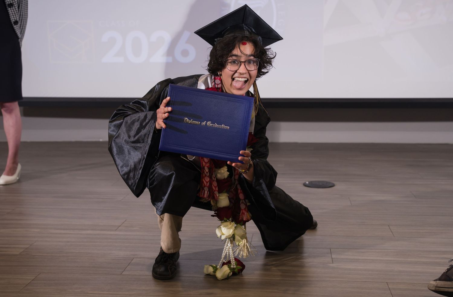 Graduate in traditional graduation regalia and turquoise jewelry celebrates during commencement ceremony.