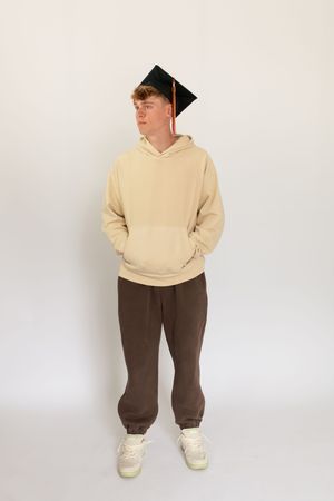 Person wearing a cream colored hoodie and brown pants with white sneakers poses against a light background.