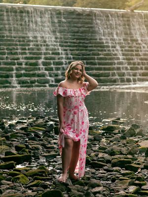 A child in a pink dress explores rocky terrain near a water feature with lily pads.