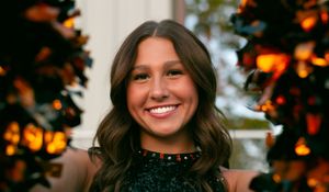 A smiling individual poses outdoors with golden autumn leaves and glowing bokeh lighting in the background.