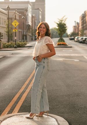Someone wearing a white blouse and light blue denim jeans poses casually on an urban street at sunset.