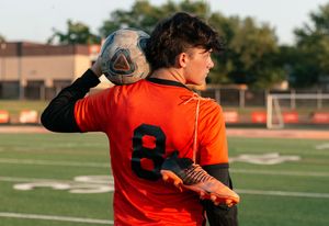 Baseball player in orange jersey makes a throwing motion during practice on a sunny day at the field.