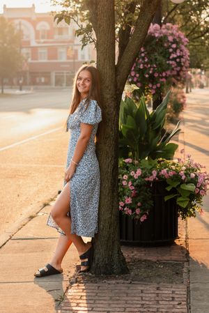 A floral dress and sandals in a golden hour moment beside blooming pink flowers and a tree.