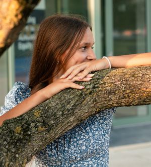 A person in a floral print dress leans against a tree trunk during golden hour lighting.
