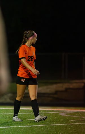 Soccer player in orange jersey number 28 and black knee socks stands on turf field during nighttime game.