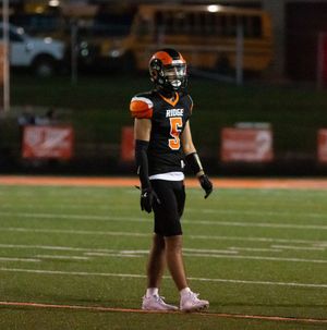 A football player in black and orange uniform stands on field wearing pink cleats during a night game.