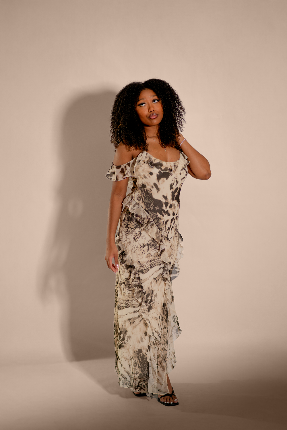 Model wearing a flowy black and white marbled print maxi dress with off-shoulder details against beige backdrop.