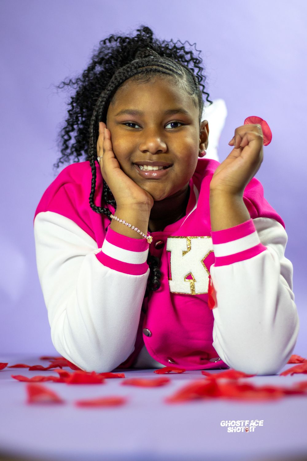 A cheerful portrait with a purple background showing a pink and white letterman jacket and red decorative touches.