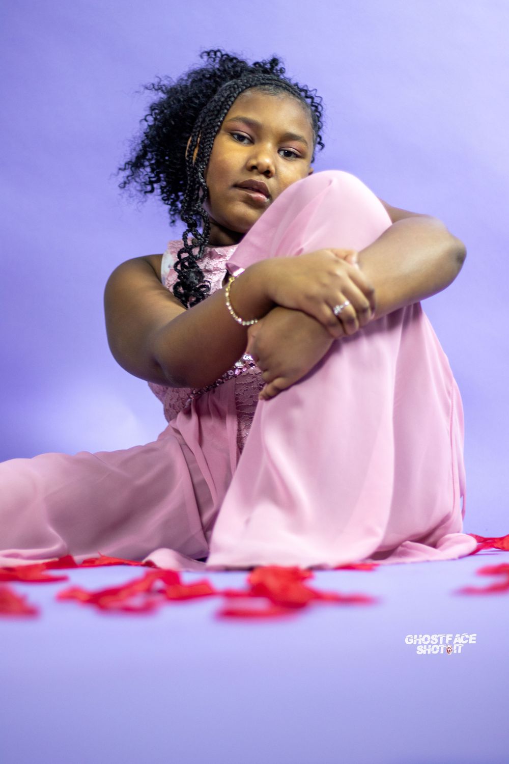 Person in pink dress poses gracefully against purple backdrop with scattered red petals.