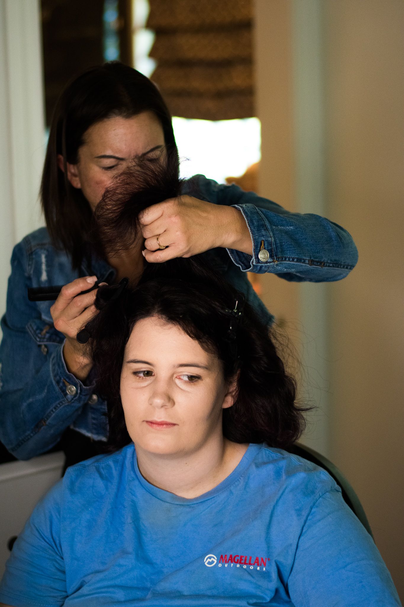 A stylist in denim separates sections and styles dark hair during a salon appointment.
