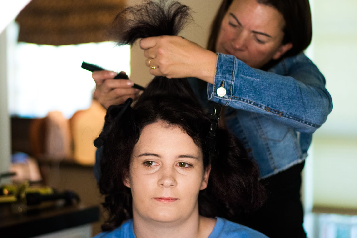 A hairdresser wearing denim works on sectioning a client's dark hair.