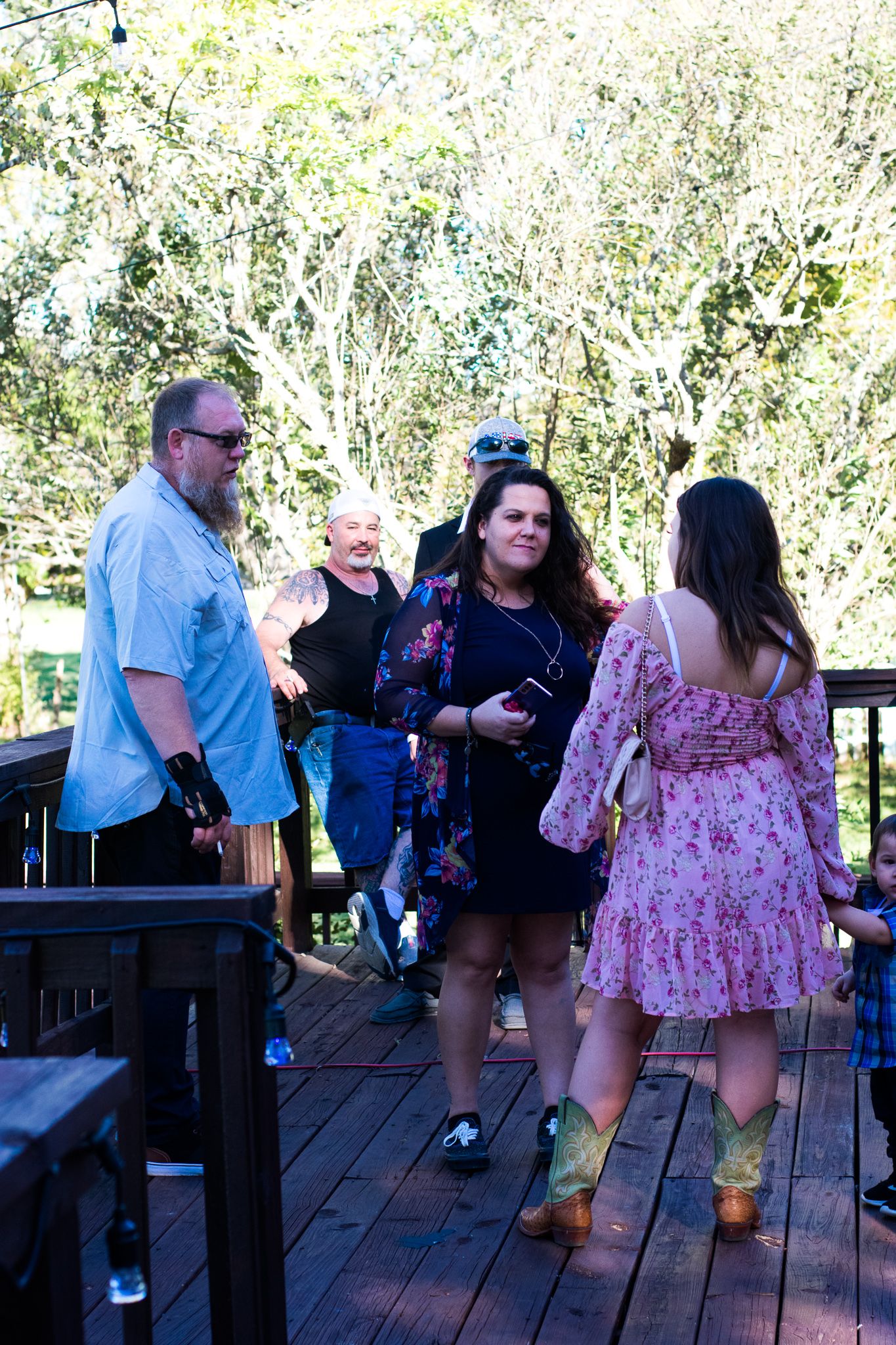 People gathered on a wooden deck having conversations on a sunny day.