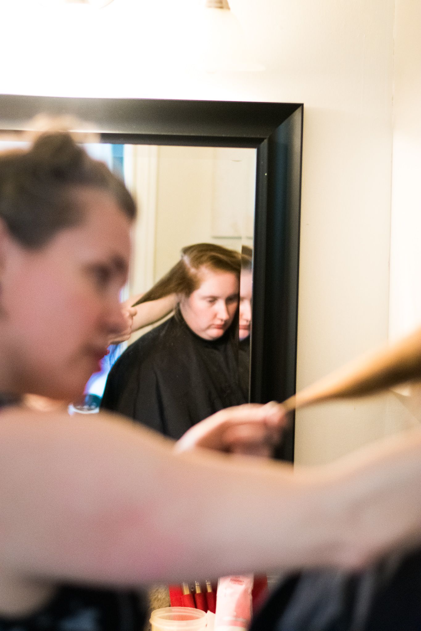 Mirror reflection during a hair styling session in a dimly lit room.