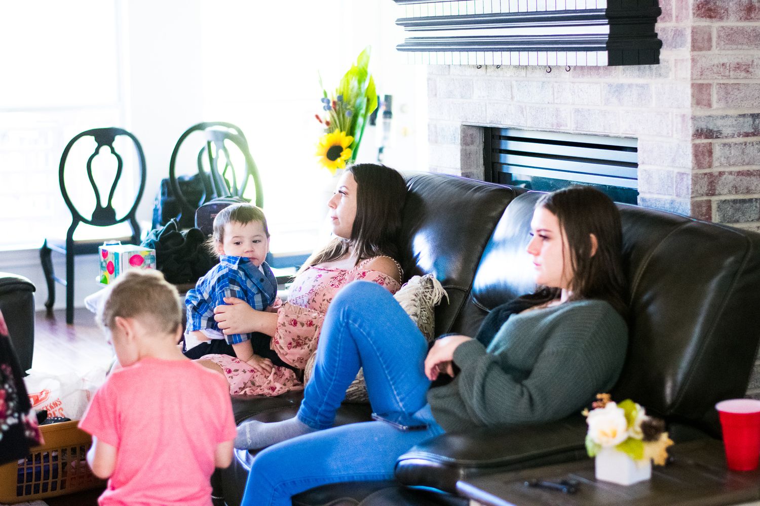 A group relaxes on a leather couch in a living room with sunflowers visible in the background.