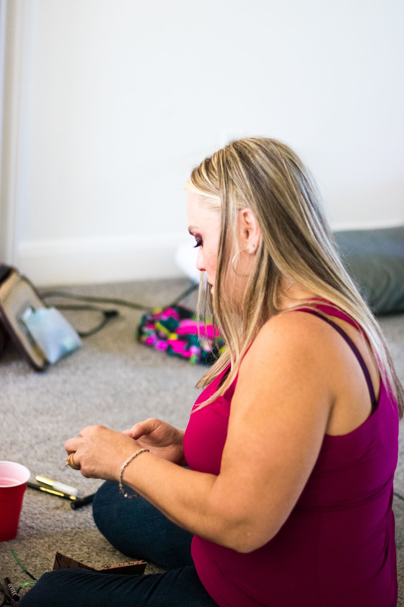 A person in a pink tank top sits on carpeted floor looking at something in their hands.