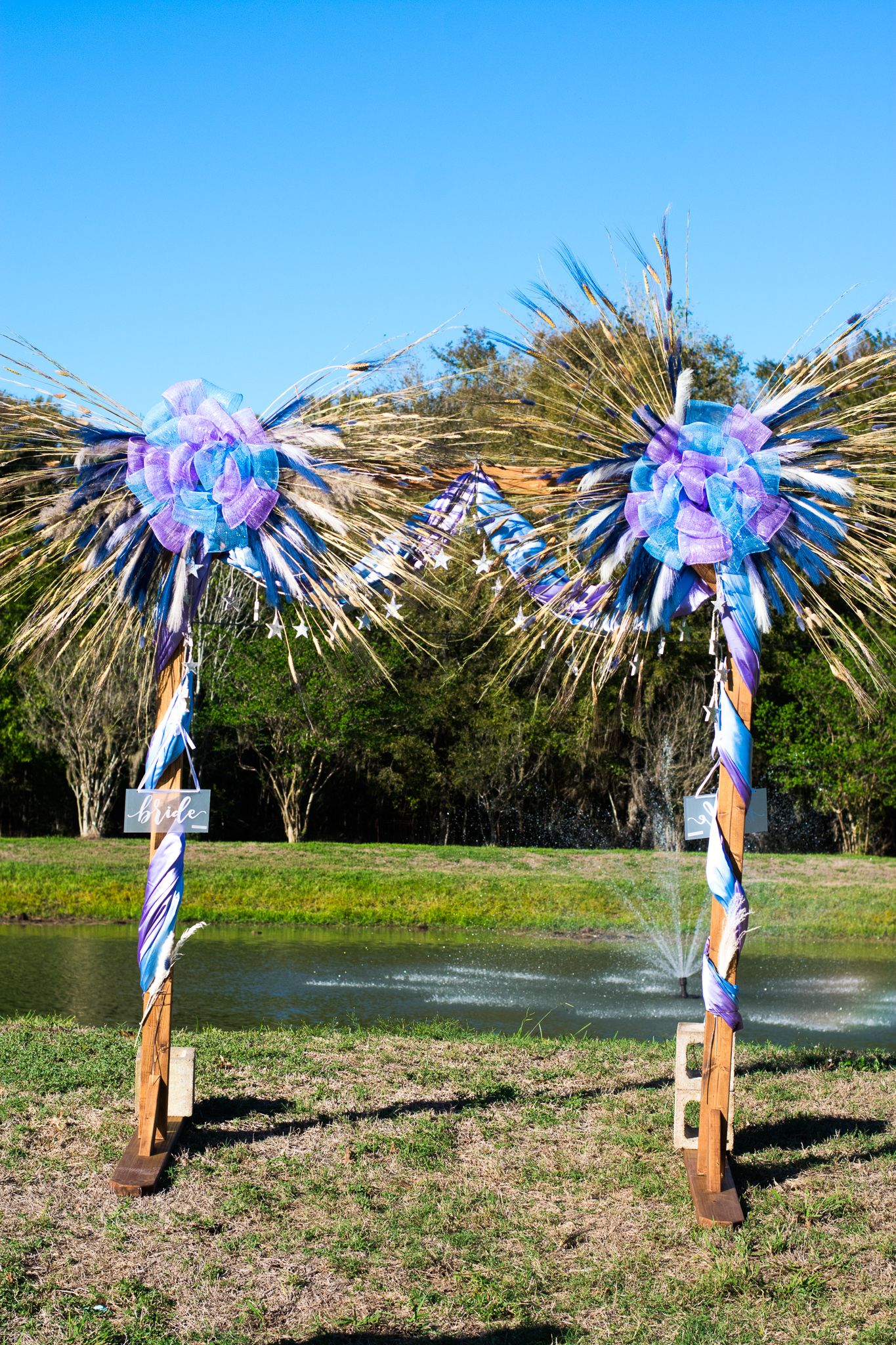 Decorative wedding arch with blue and purple flowers against a bright sky.