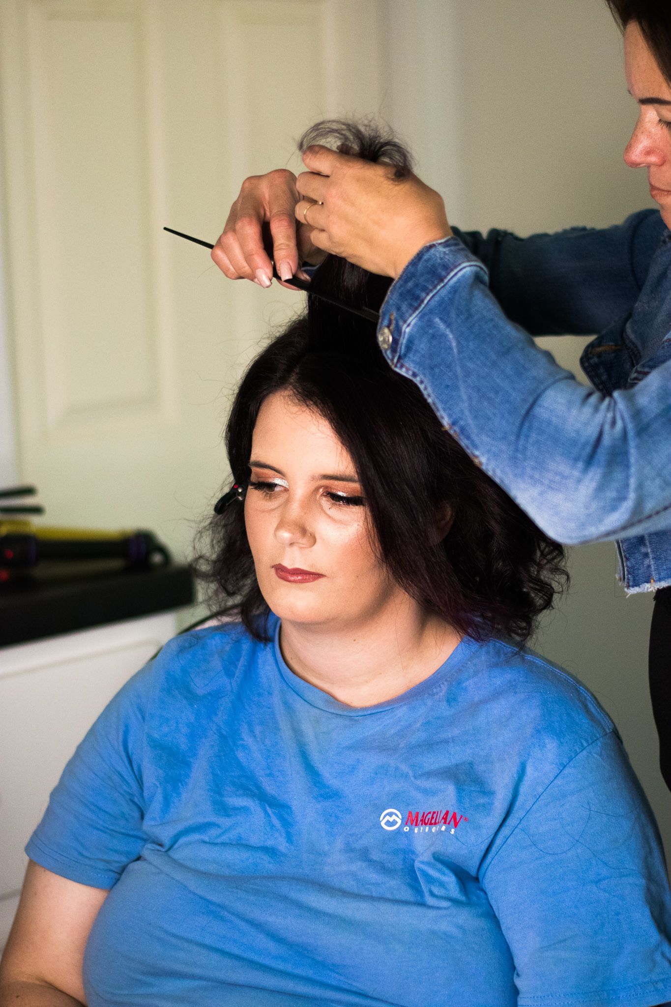 A stylist working on a client's dark hair while wearing a denim jacket.