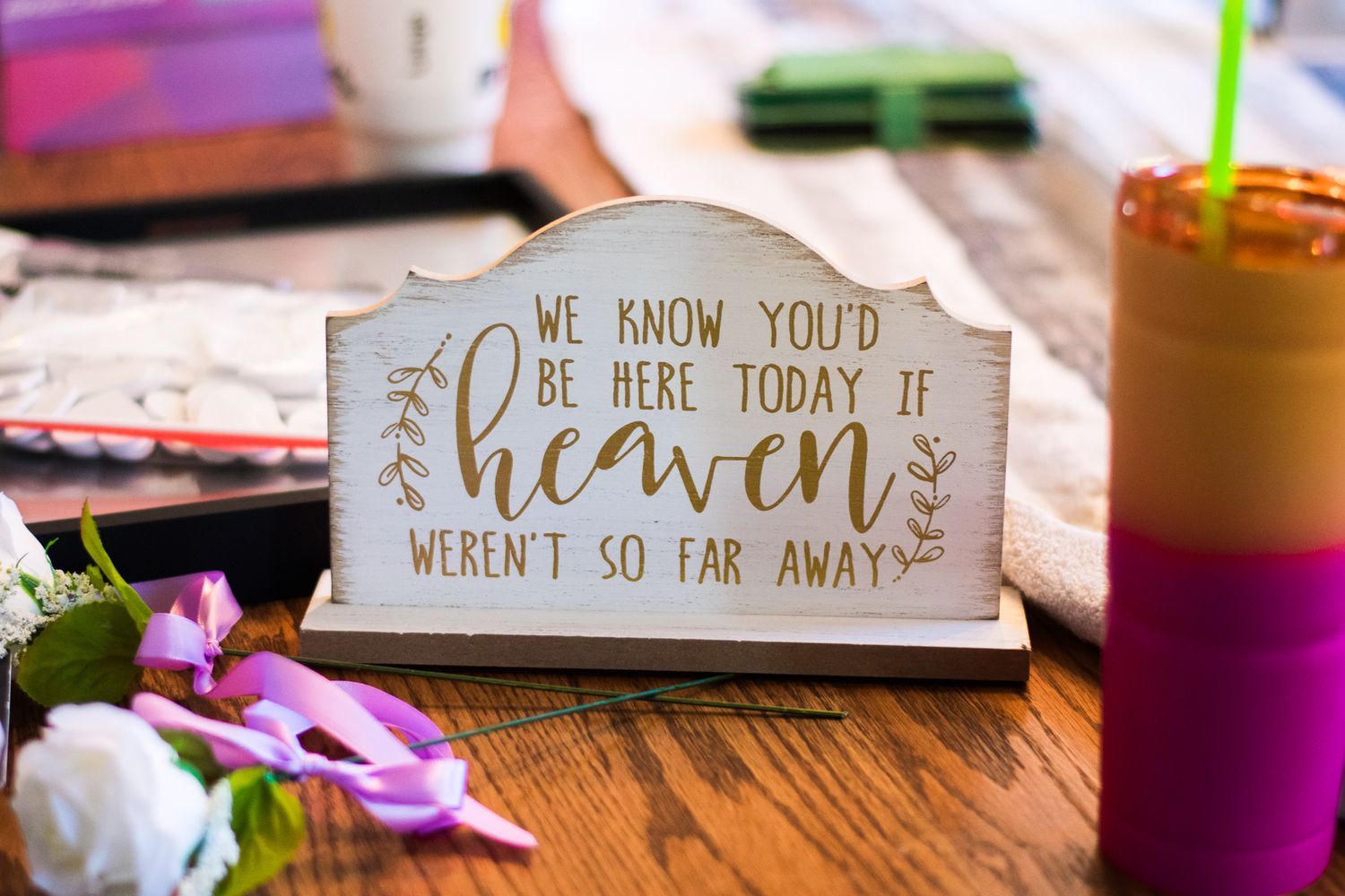 A wooden sign with cursive text reading 'We know you'd be here today if heaven weren't so far away'.