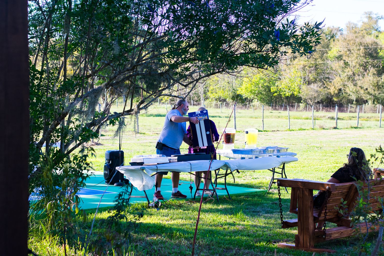 People enjoying an outdoor gathering with picnic tables and seating in a sunny park setting.