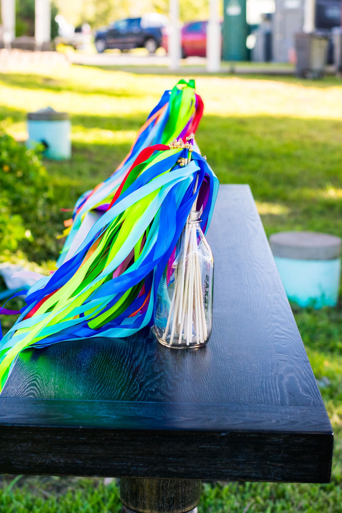 Colorful rainbow ribbons and tassels decorating a dark wooden table at an outdoor event.