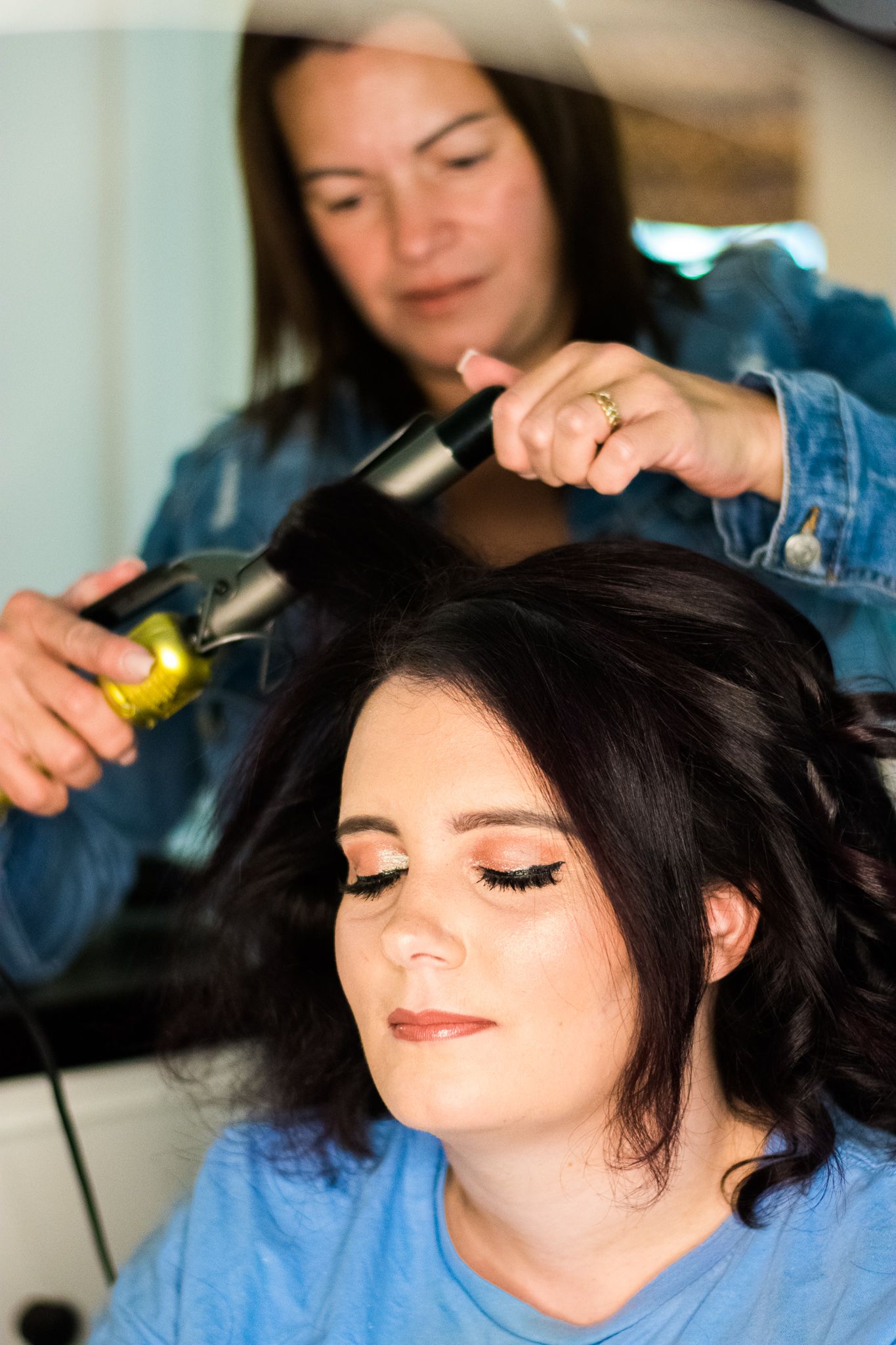 Hairstylist using curling iron on dark hair during wedding preparation.
