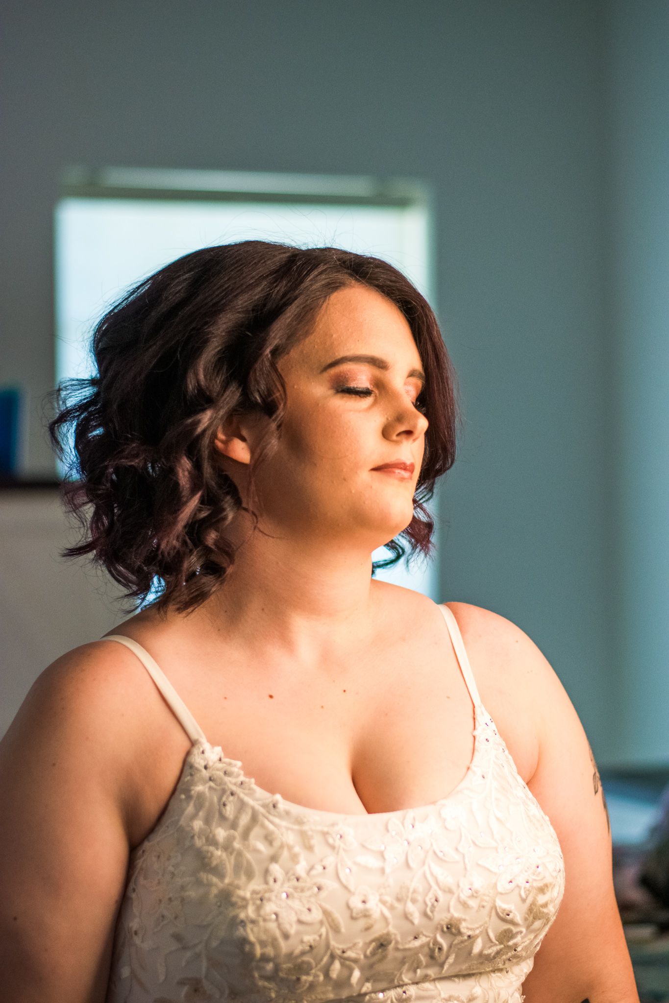Person in white lace spaghetti strap top with curly purple-tinted hair during a photoshoot.