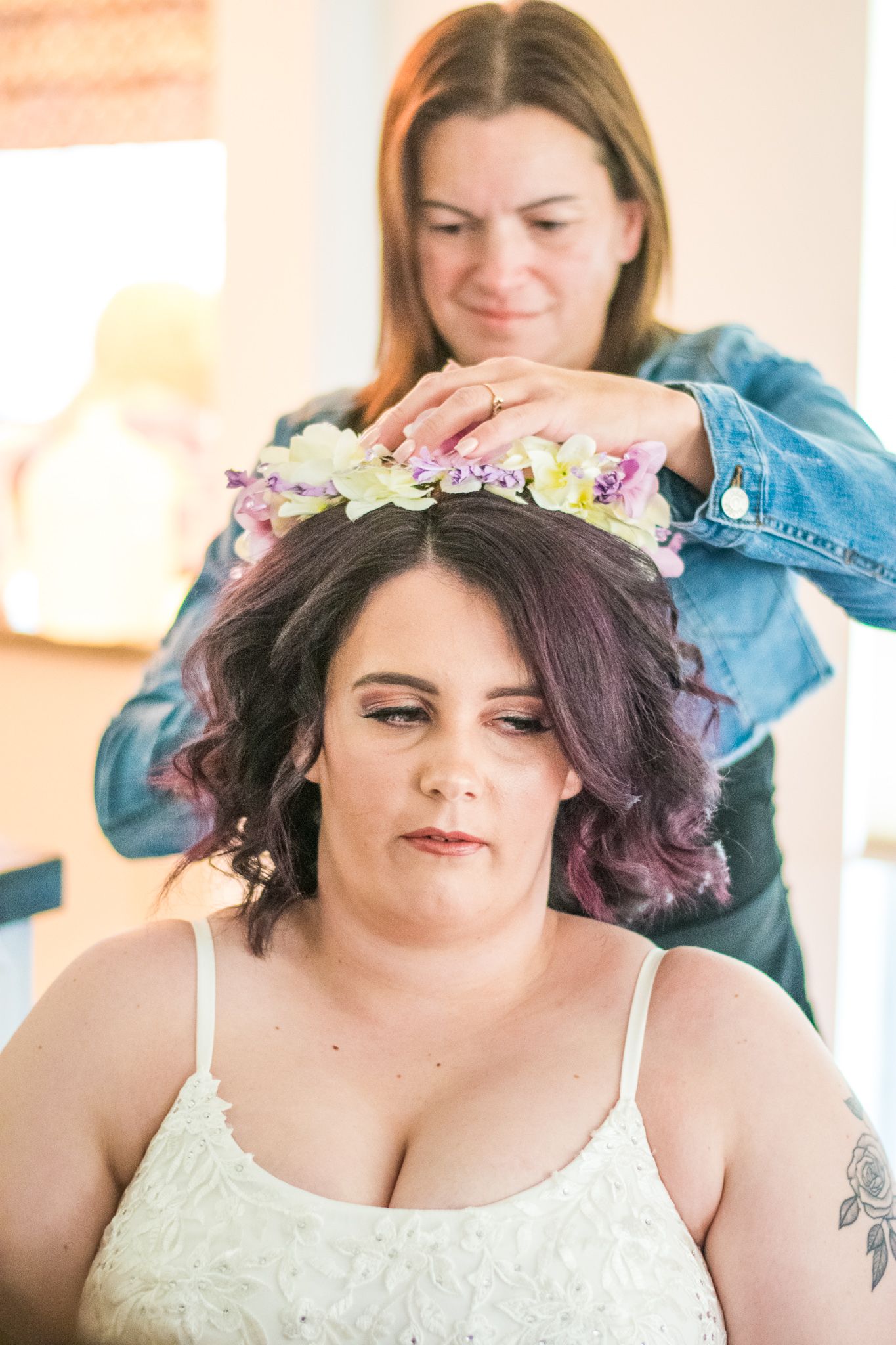 Stylist placing delicate floral crown on client wearing white top during wedding preparation.
