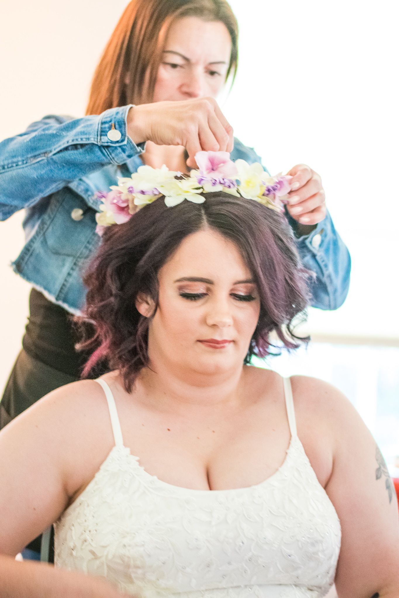 Floral crown being placed on purple-tinted curly hair during bridal preparation.
