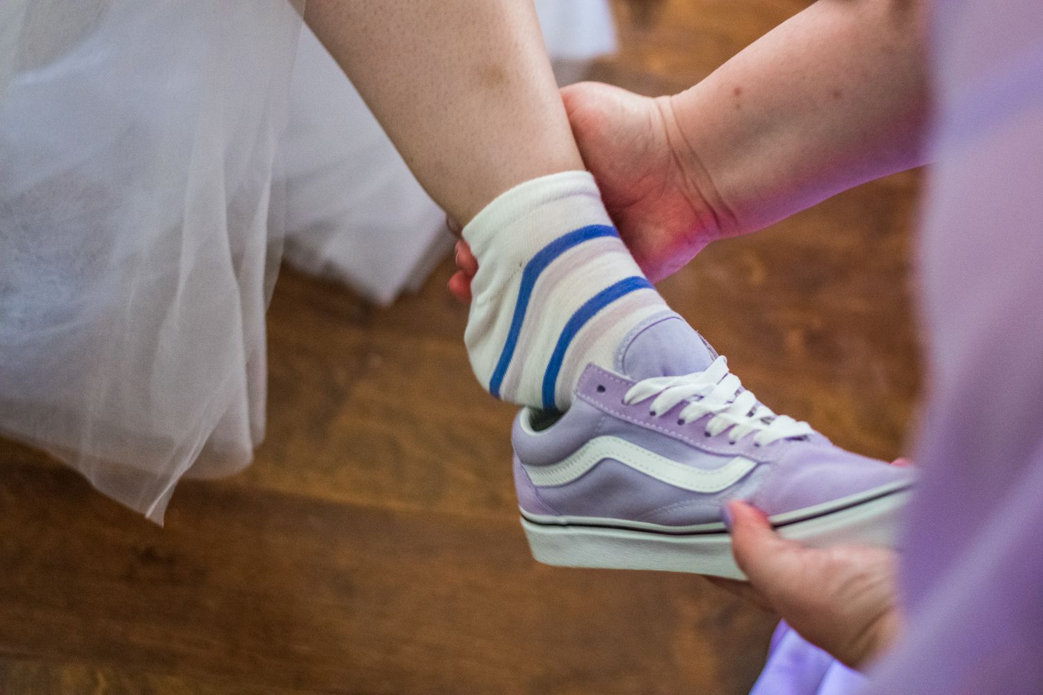 Purple and white Vans sneakers shown with striped socks under tulle fabric.
