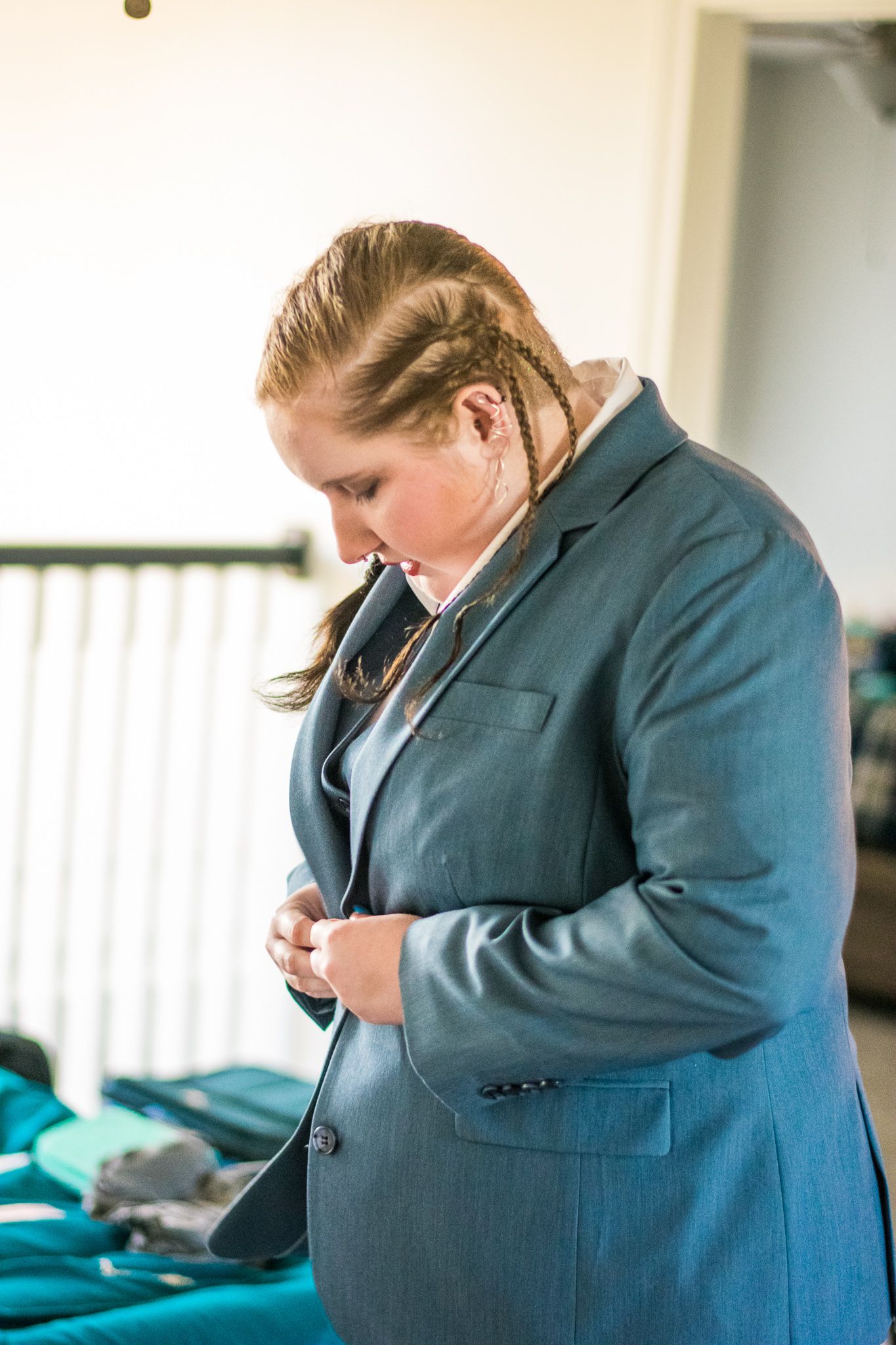 Person adjusting buttons on blue formal suit with side-braided hair.