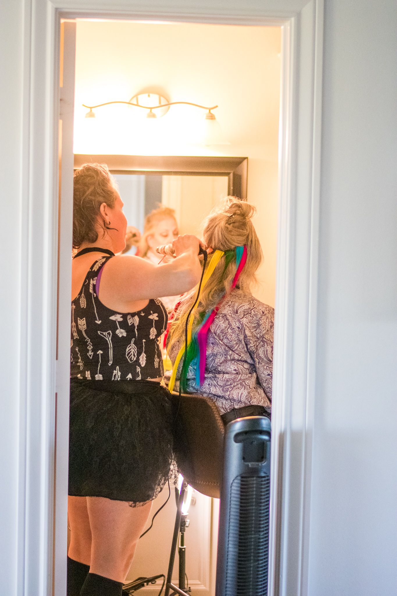Wedding party gets ready in a bright bathroom with decorative lighting fixture.