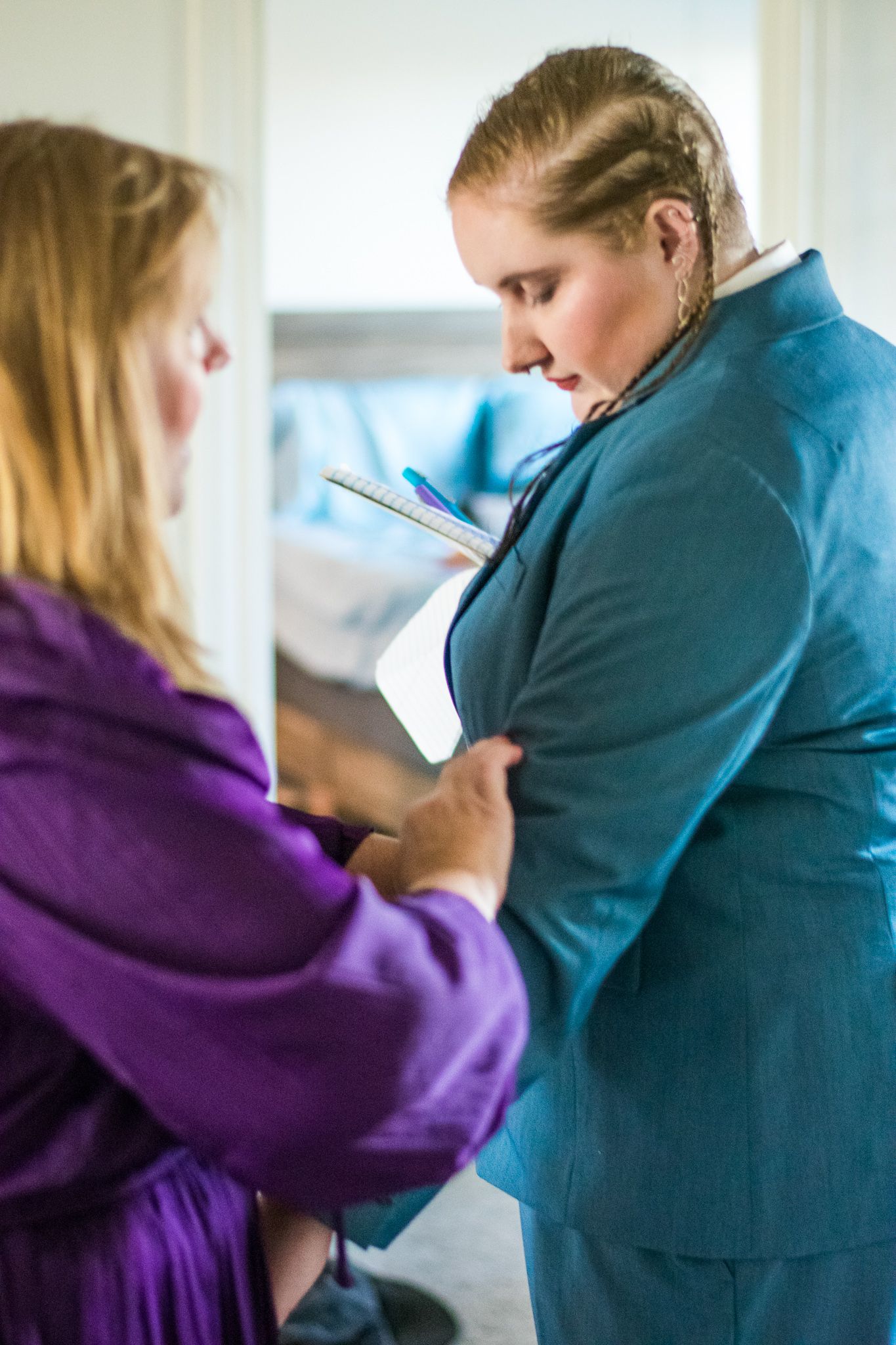 Two people review notes while getting dressed in formal attire.