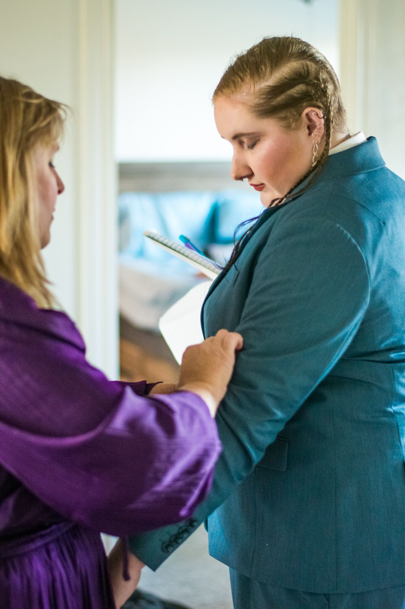 Someone in a purple robe helps adjust clothing on another person in teal.