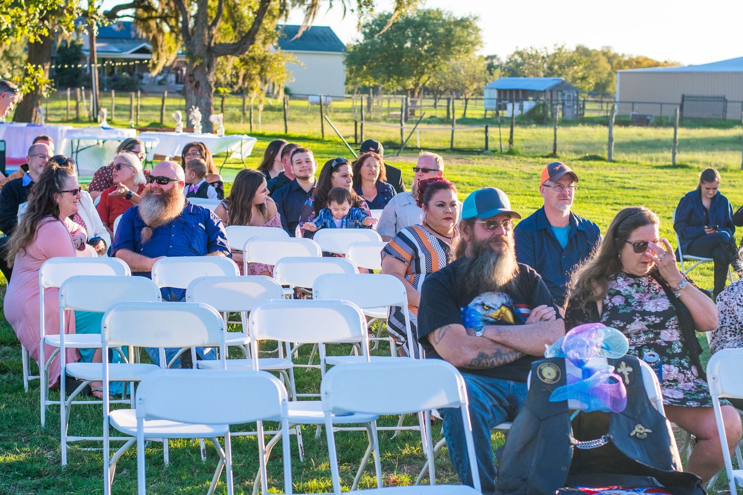 Guests seated at white folding chairs for an outdoor event at sunset.