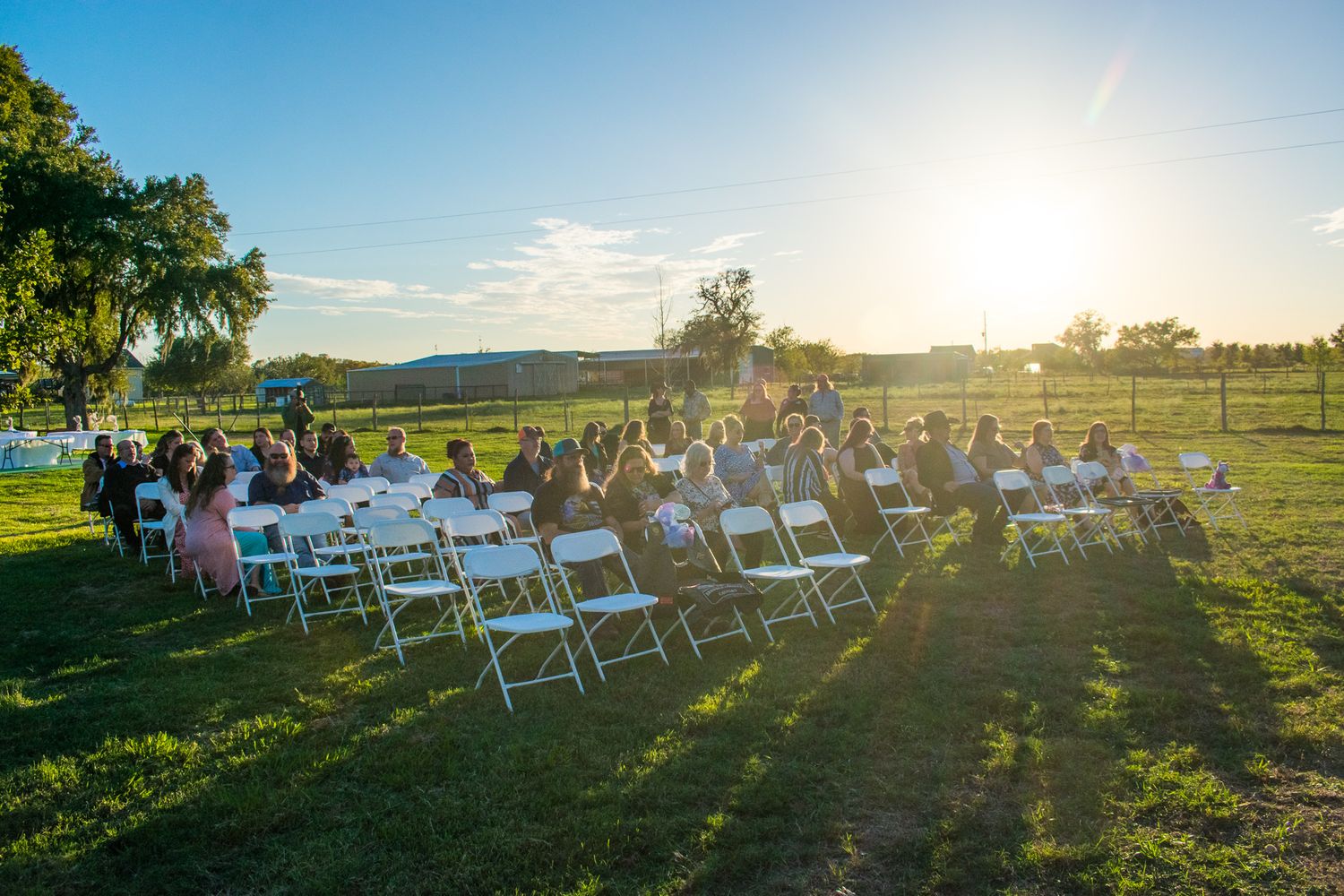 White folding chairs set up for outdoor ceremony with golden sunlight streaming through trees.