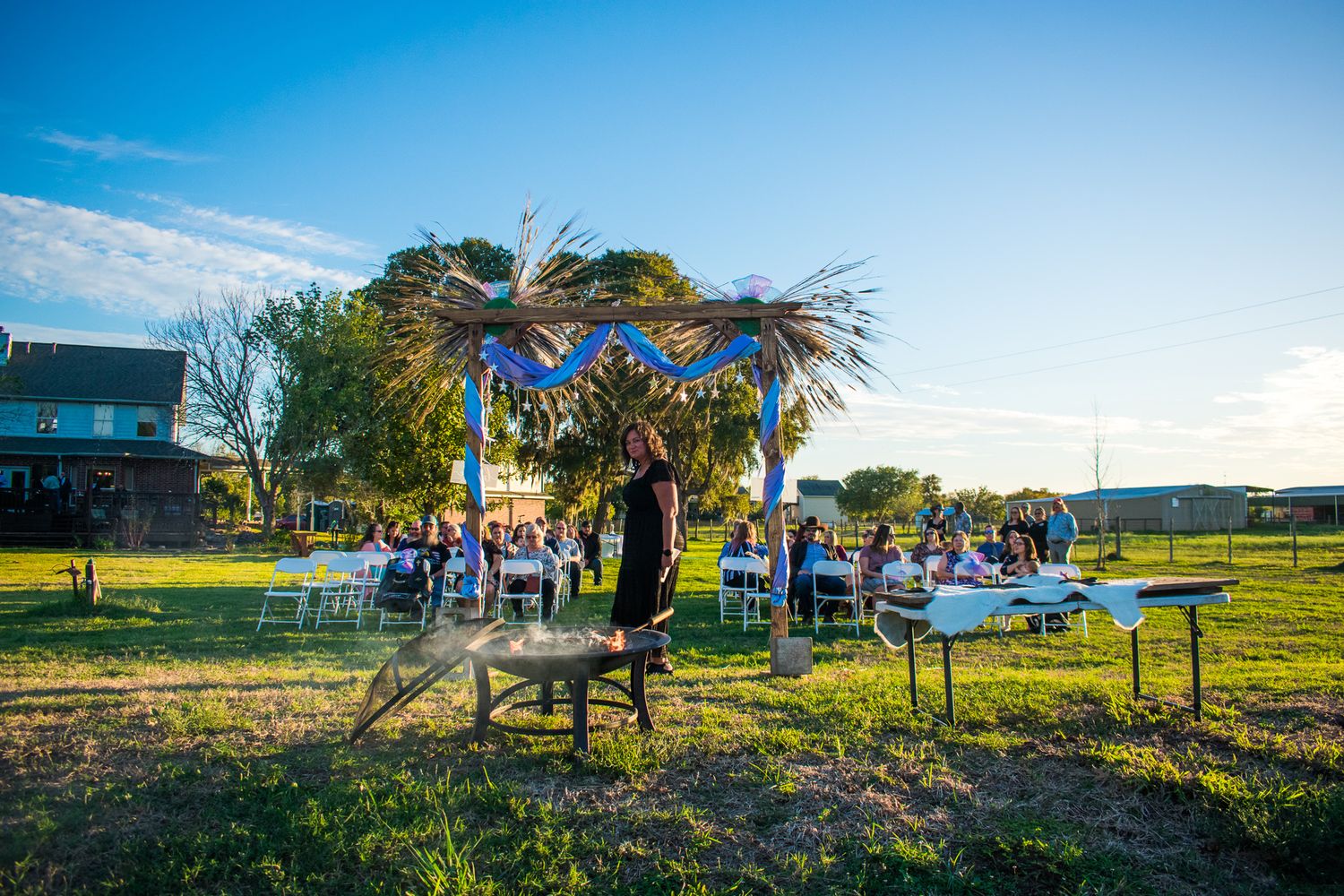 Rustic outdoor wedding ceremony setup with decorated arch and white chairs.