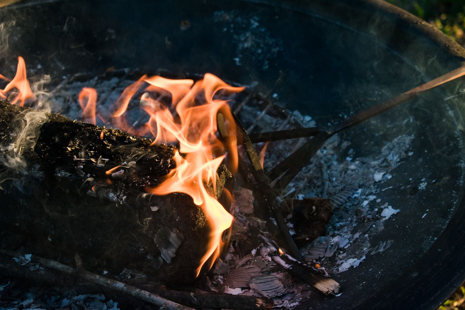Bright orange flames dance in a dark fire pit during evening gathering.
