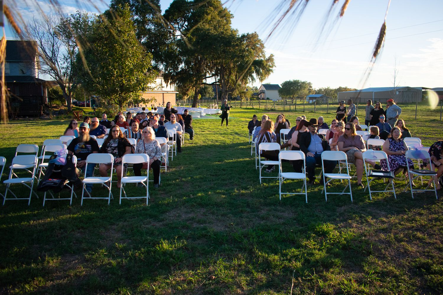 Rows of white chairs arranged outdoors on grass for a garden wedding ceremony during golden hour.