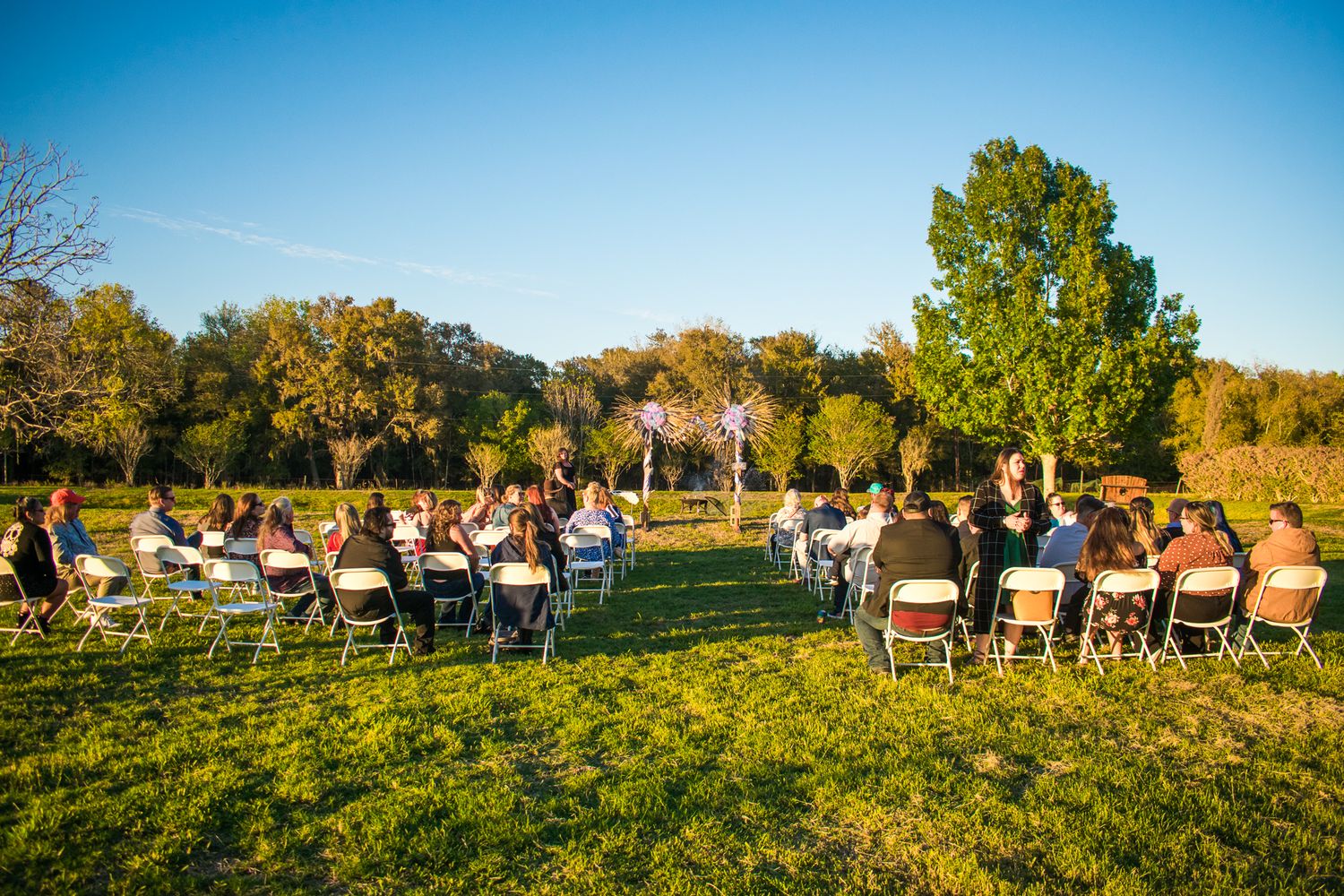 Outdoor wedding ceremony setup with white chairs on a grassy lawn surrounded by autumn trees.