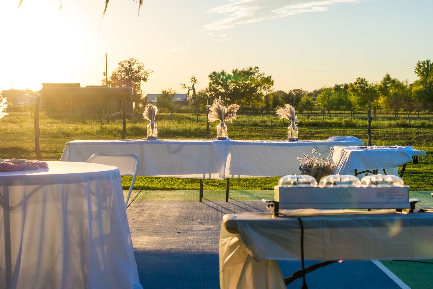 Outdoor buffet tables set up at sunset with white tablecloths and serving stations.