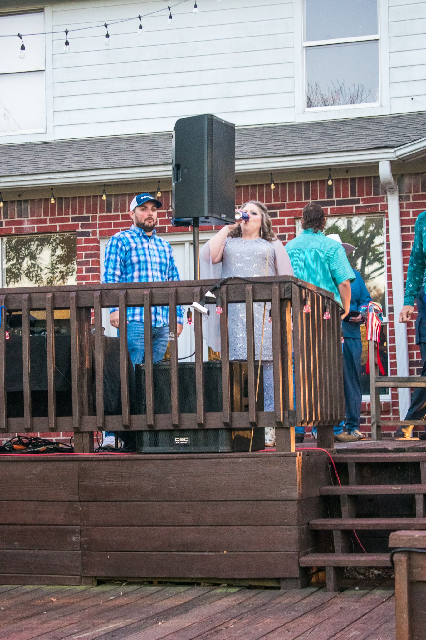 People socializing on a raised wooden deck with string lights and speakers.