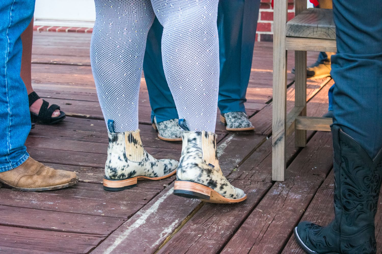 Close-up of cowboy boots and patterned tights on a wooden deck.