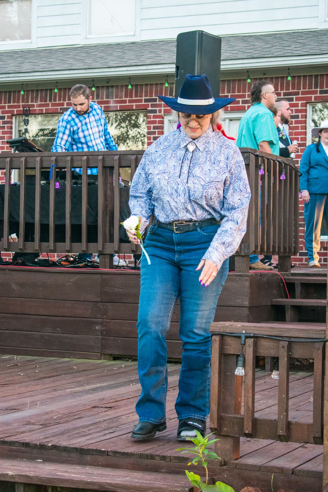 Person in western wear with blue jeans and cowboy hat standing on wooden deck.