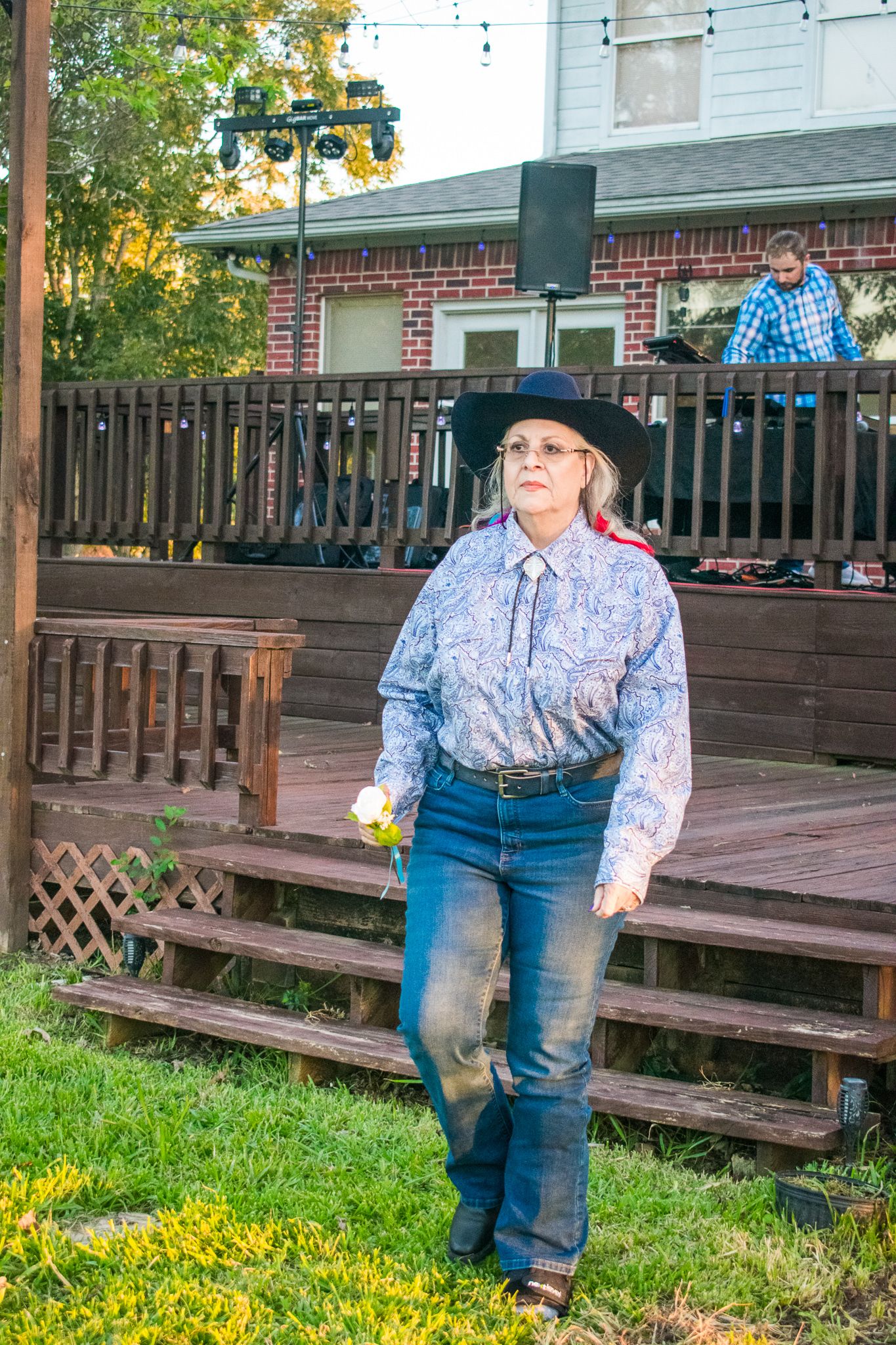 Person in cowboy attire posing on wooden deck with brick building in background.