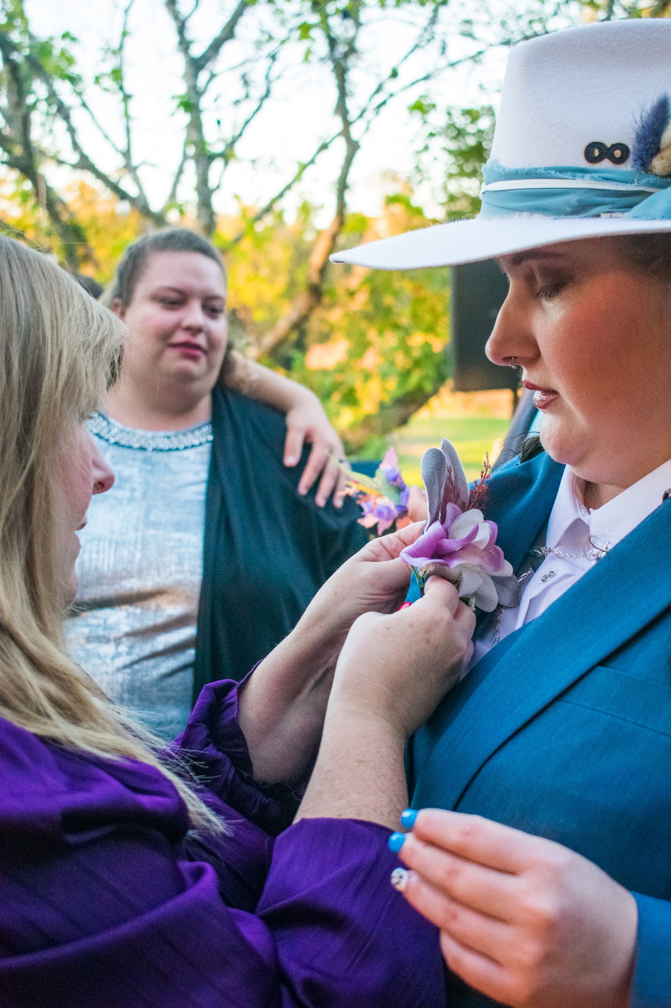 Person in blue suit and white hat receiving purple corsage outdoors.