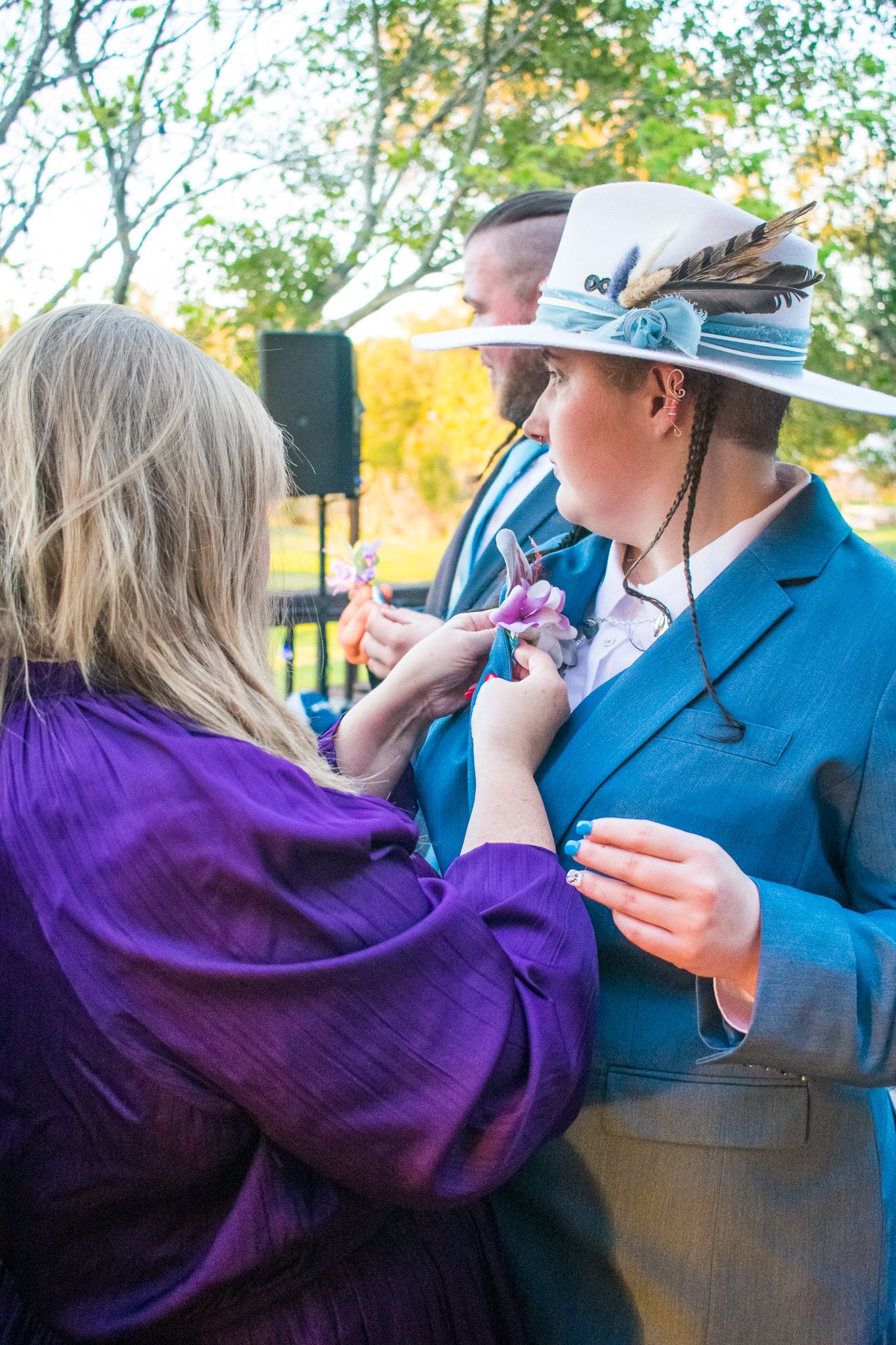 Person in blue suit and white hat having purple corsage pinned on.